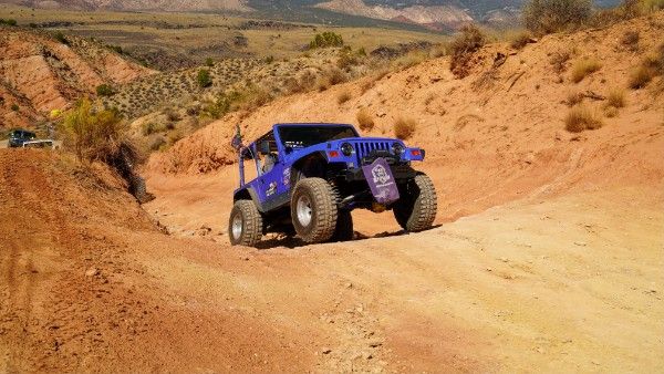 Betty Lou, a blue 1997 Jeep Wrangler, coming down an orange dirt wash with desert hills behind it
