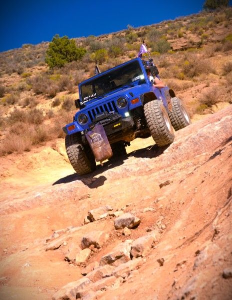 Betty Lou, a blue 1997 Jeep Wrangler, angled up a steep sandstone slope with its front tire lifted