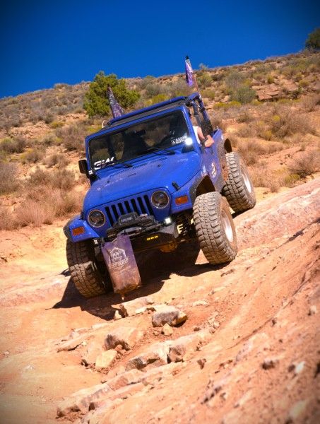 Betty Lou, a blue 1997 Jeep Wrangler, climbing a steep slickrock ledge under a deep blue sky