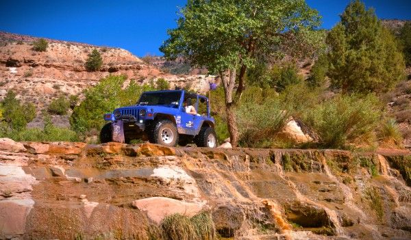 Betty Lou, a blue 1997 Jeep Wrangler, parked on a layered rock ledge beside a cottonwood tree